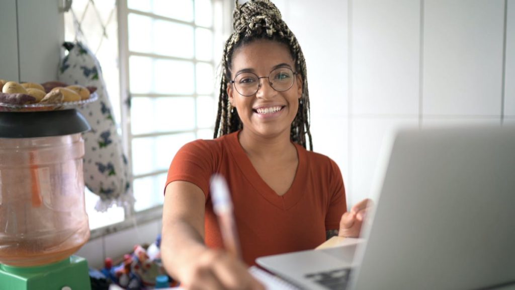 mulher sorrindo com caneta na mão em frente ao computador: diferença entre bacharelado e licenciatura
