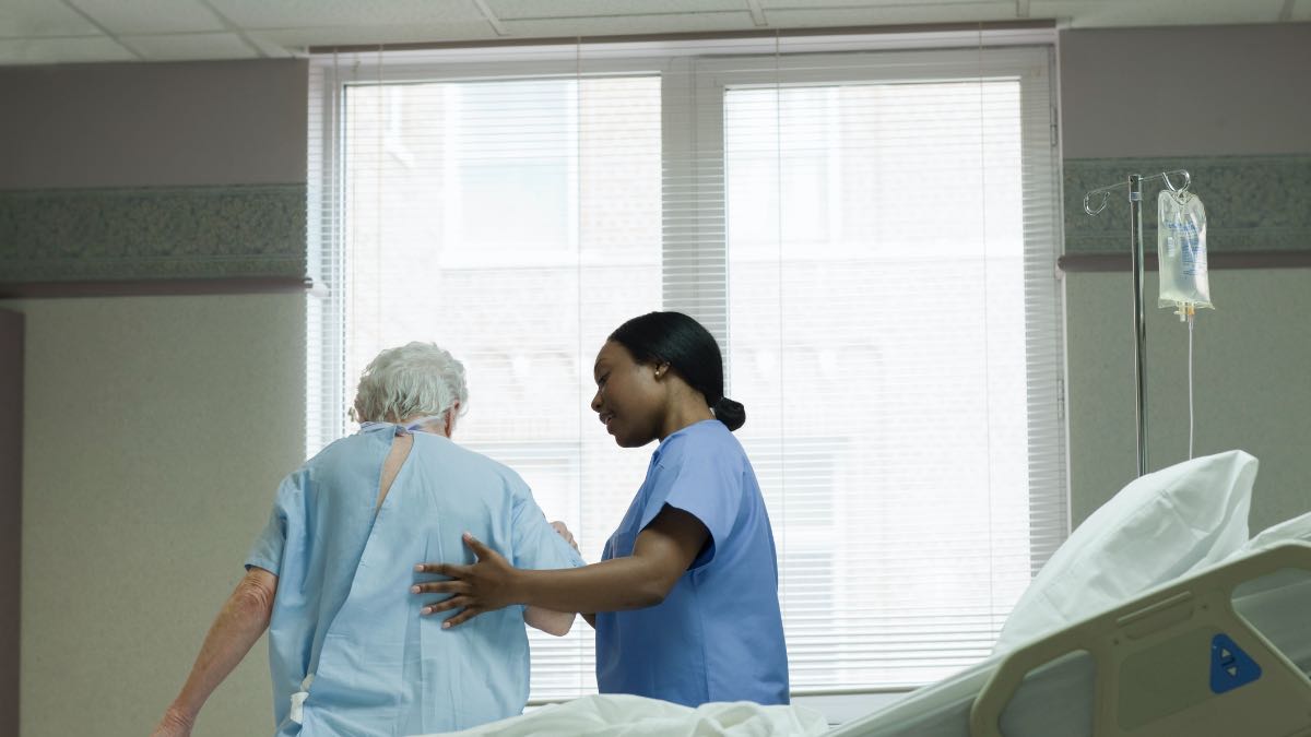 enfermeira ajudando idosa a caminhar: quanto custa uma faculdade de enfermagem